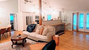A spacious living room with a sofa, coffee table, and a dining area with chairs. There is a kitchen in the background with cabinets and a refrigerator. - Spacious Pawtuckaway Getaway (Nottingham)