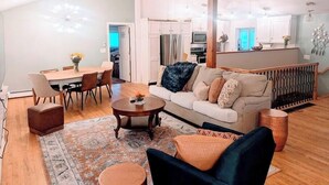 A spacious living room with a sofa, coffee table, and dining area. There is a kitchen in the background with white cabinets and a microwave. - Spacious Pawtuckaway Getaway (Nottingham)