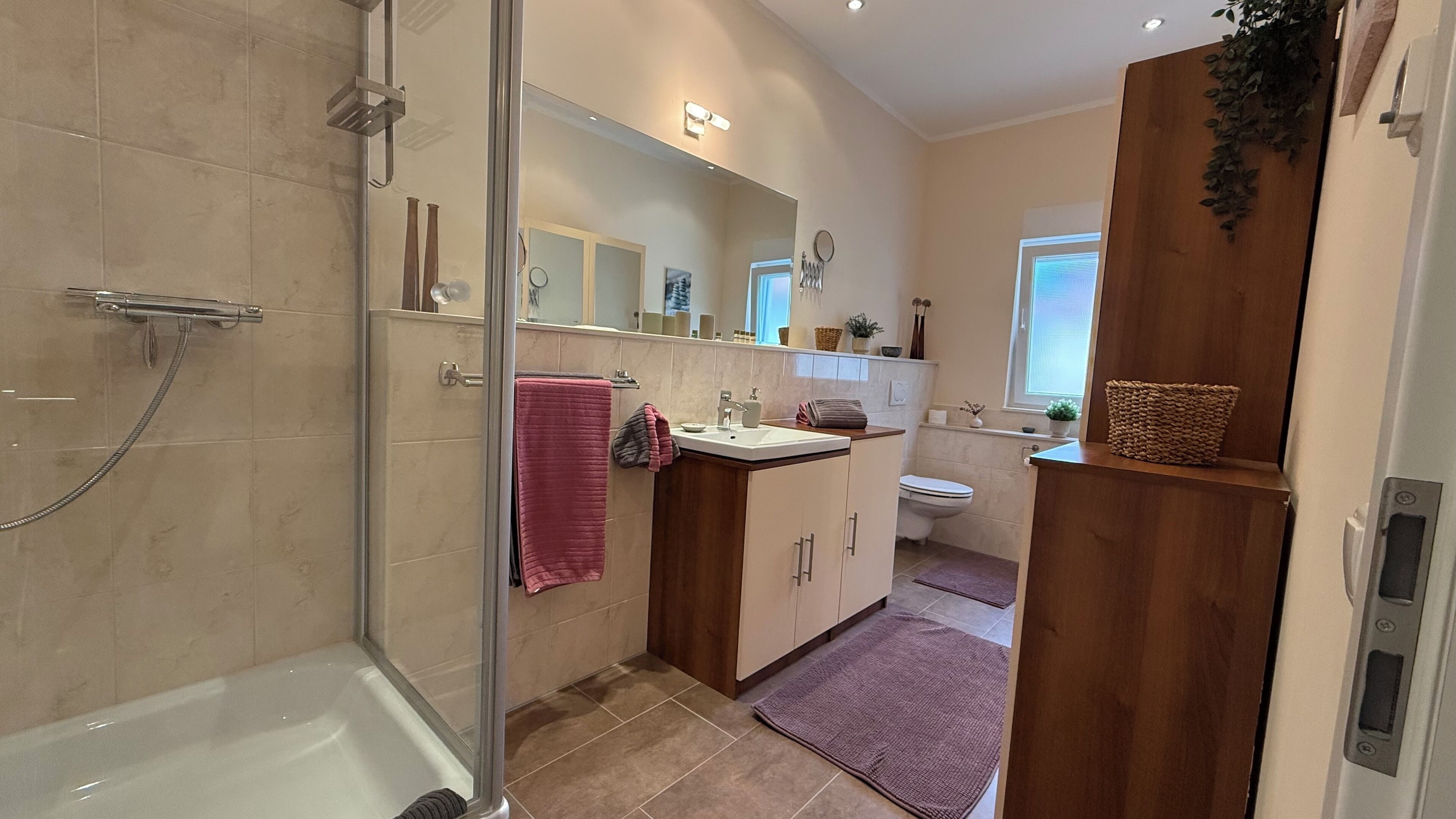 A modern bathroom with a glass shower enclosure, a white bathtub, a wooden vanity with a sink, and a toilet.