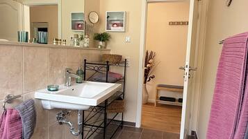 A modern bathroom with a white sink, mirror, and tiled floor. There is a black rug in the center, and towels are hung on the wall.