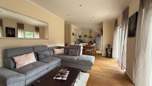 A modern living room with a grey sectional sofa, a wooden coffee table, and a kitchen in the background. - Enjoy KRK waterfalls, sun, beach and sea: Domicile Sunce Krka Studio (Skradin)
