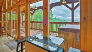 A wooden cabin with large windows, a glass bar counter, and a deck with a view of the outdoors. - Awesome Private Mountain views Resort Pool &HotTub (Sevierville)