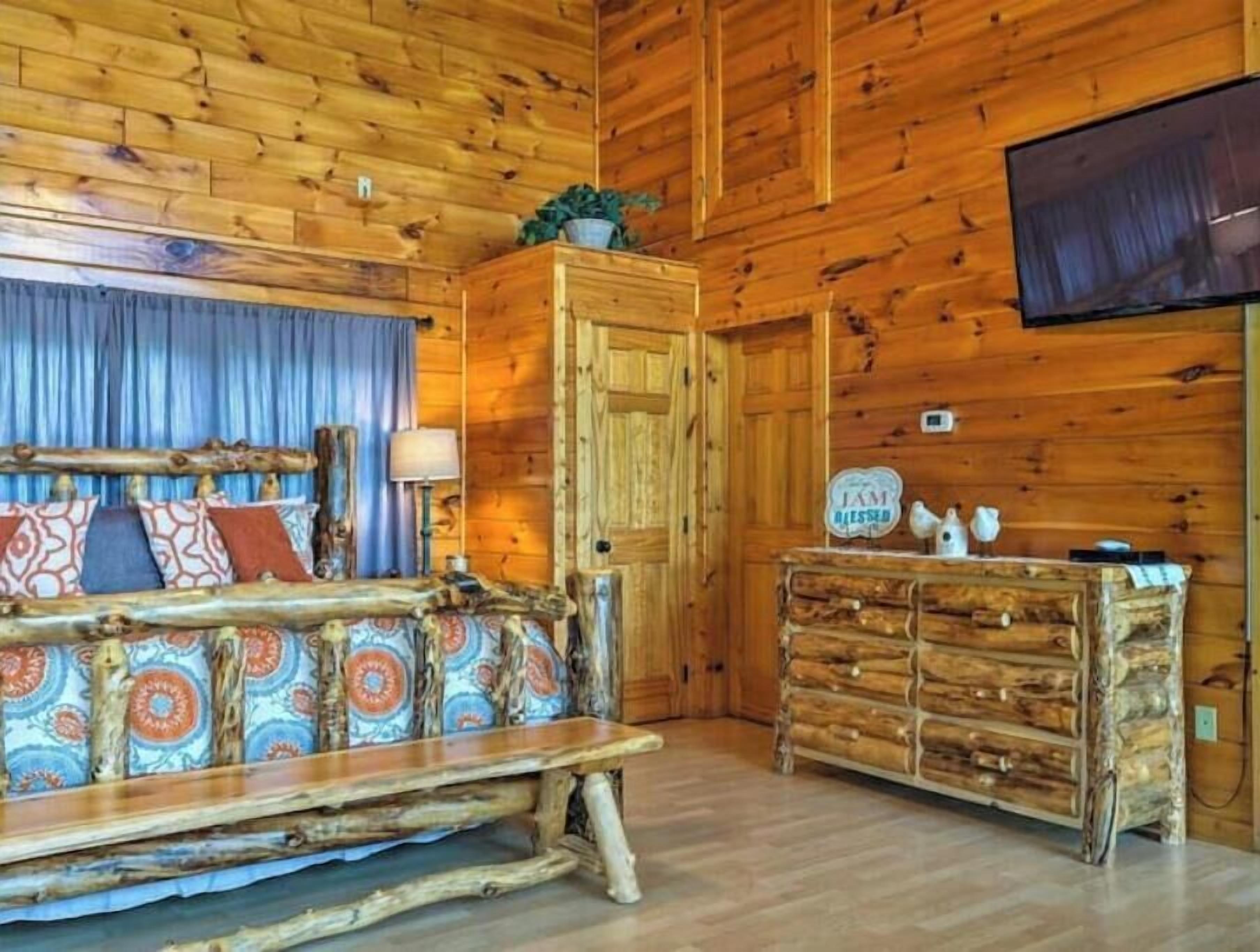 A rustic wooden room with a wooden bench, a dresser, and a television mounted on the wall.