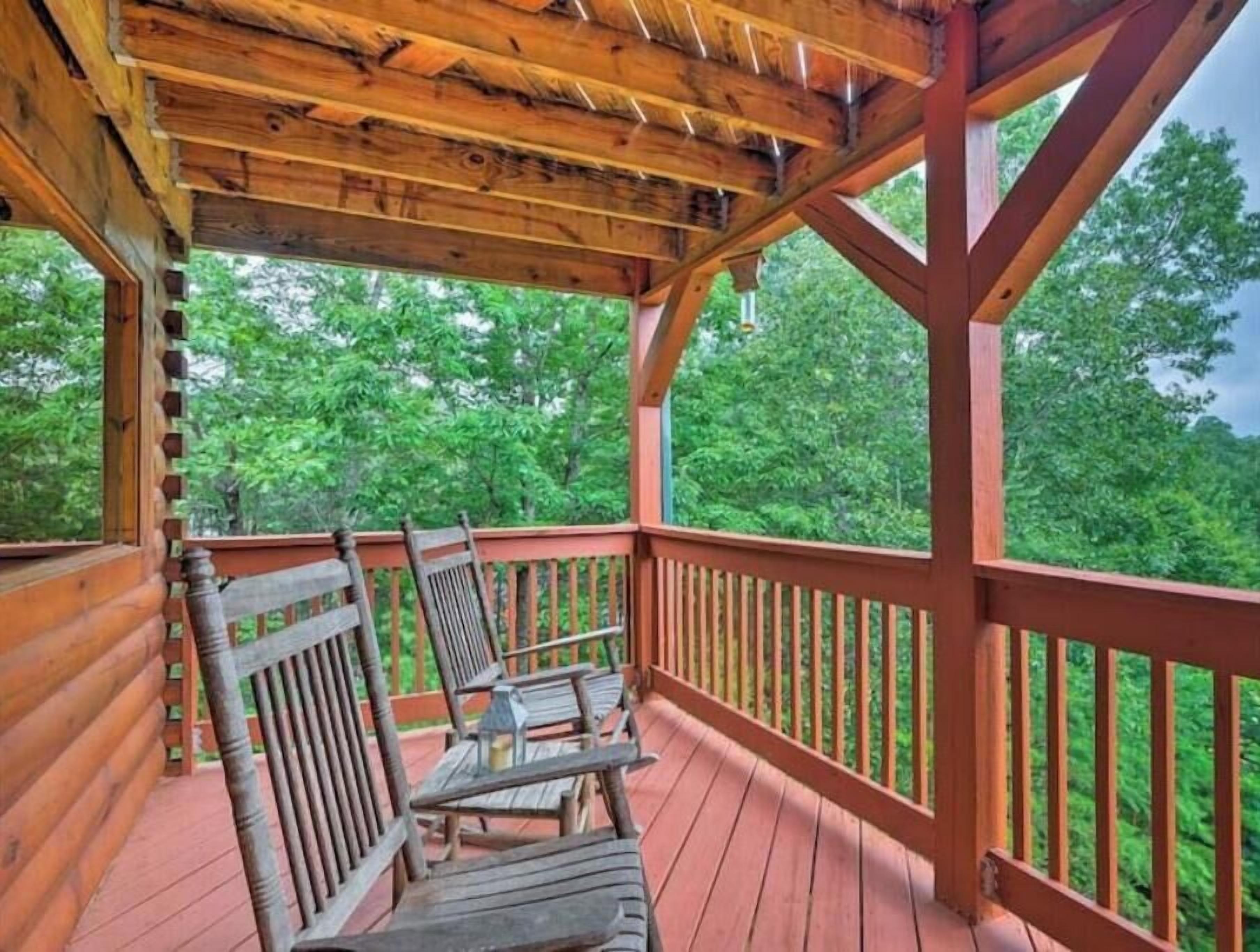 A wooden deck with a covered area, featuring two wooden chairs and a small table.