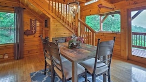 A wooden cabin interior with a dining table, chairs, a staircase, and a view of the outdoors. - Awesome Private Mountain views Resort Pool &HotTub (Sevierville)