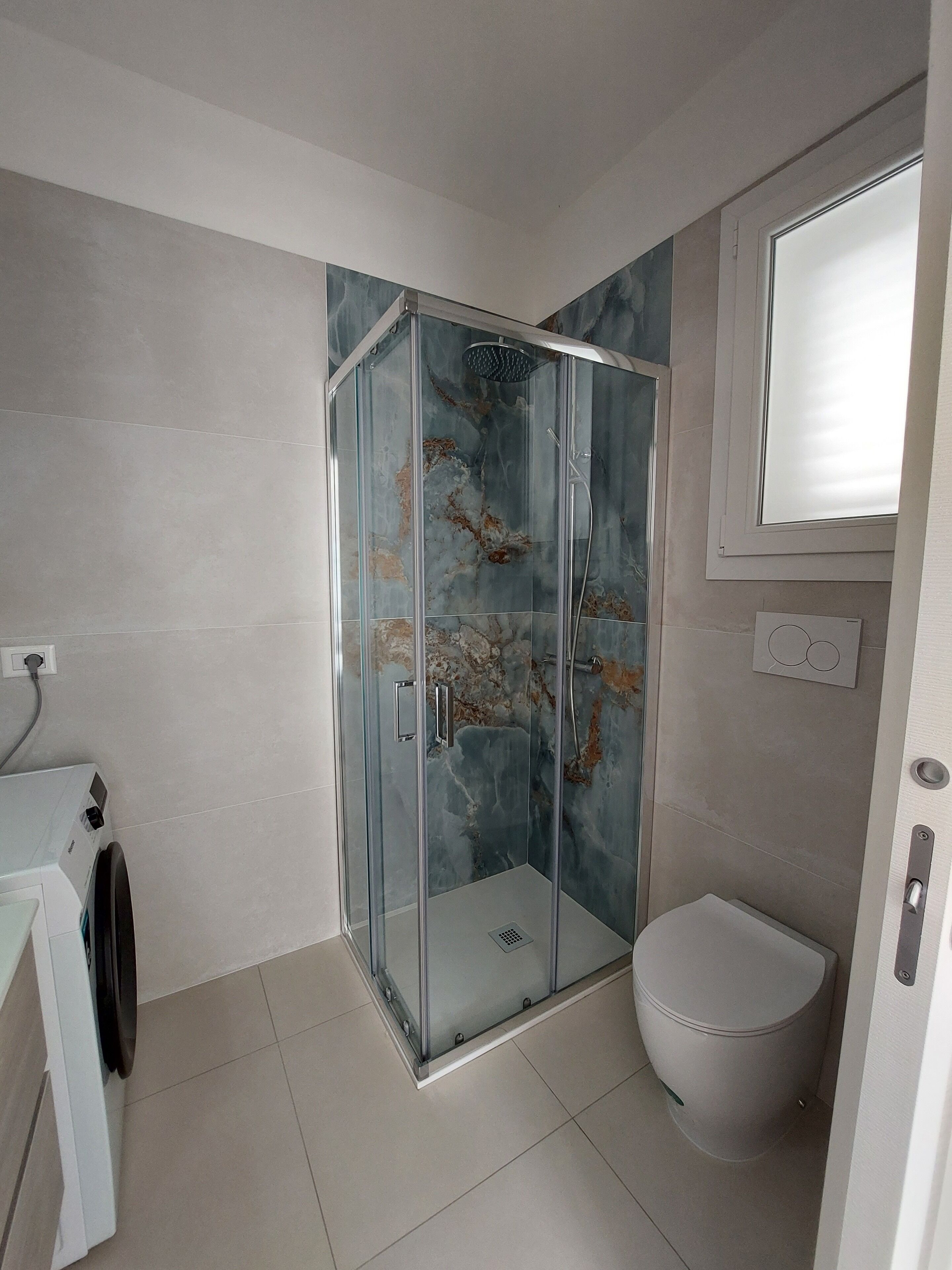 Un baño moderno con ducha envuelta en vidrio, inodoro y lavabo con lavadora.