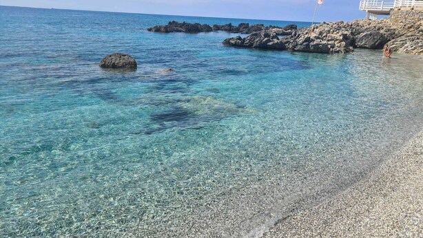 Una playa despejada con formaciones rocosas y un edificio con balcón que da al mar.