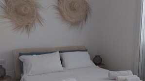 Una cama bien hecha con ropa blanca y toallas enrolladas, un cabecero de madera y dos cuadros colgados en la pared.