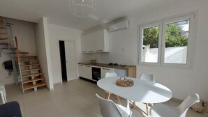 Una cocina moderna con armarios blancos, una escalera de madera y una zona de comedor con sillas blancas y una mesa redonda.