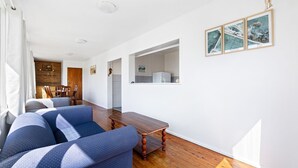 A modern living room with a sofa, wooden coffee table, and a view of the kitchen. - The Narooma Escape (Narooma)