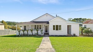 A single-story white house with a front porch, a small attached garage, and a well-maintained lawn. - The Narooma Escape (Narooma)