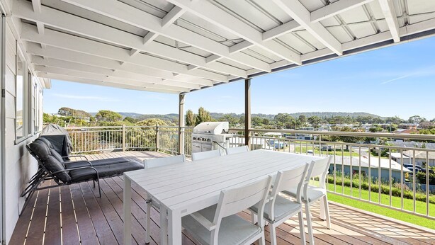 A covered outdoor area with a table and chairs, a grill, and a view of a residential area. - The Narooma Escape (Narooma)