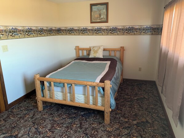 Un dormitorio con cama de madera, alfombra estampada, un mural en la pared y una ventana con cortinas.