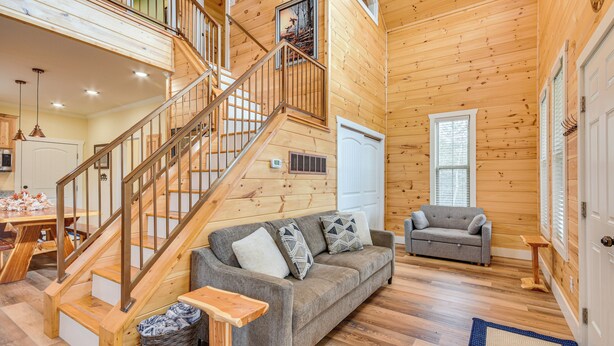 A wooden cabin interior with a staircase, a sofa, a small table, and a door.