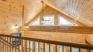 A wooden interior with a sloped ceiling, a staircase, and large windows.