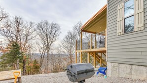 A house with a deck, a grill, and a view of trees.