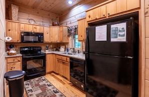 A compact kitchen with wooden cabinets, a black refrigerator, a microwave, an oven, and a dishwasher. - Bear Tree-Pet Friendly, Private Luxury Cabin Rental, 30 Minutes to the Great Smoky Mountains, Rafting-Nantahala NC (Topton)