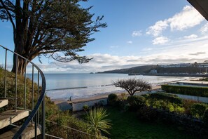 A coastal view from a balcony with a spiral staircase, overlooking a beach and a distant town. - Beach Retreat - Sea Views Parking Beach Access (Saundersfoot)