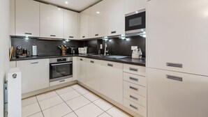 A modern kitchen with white cabinets, a black countertop, and stainless steel appliances. - 12 Rhodewood House - Near the Beach Sea Glimpses (Saundersfoot)