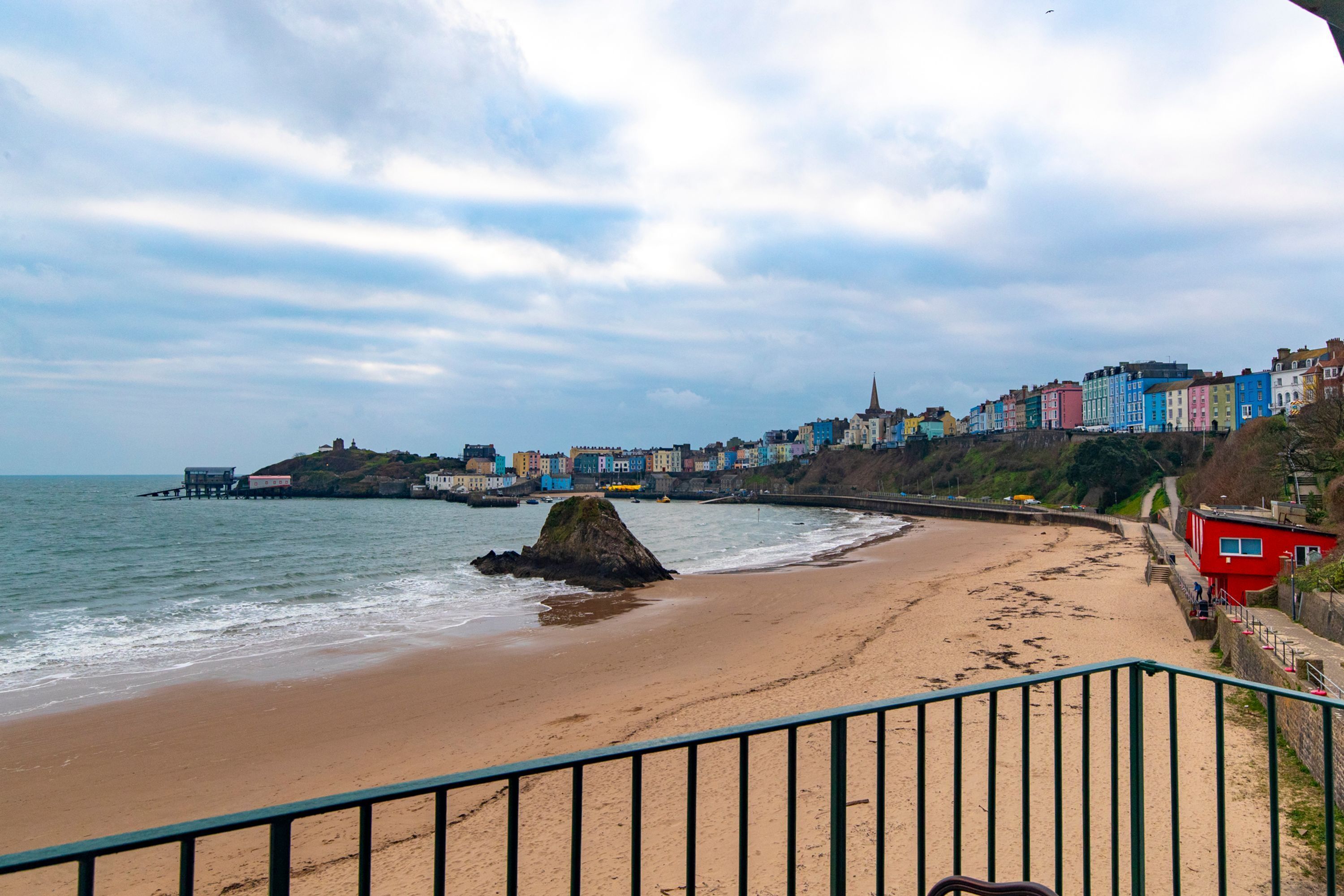 A coastal town with a sandy beach, colorful buildings, and a pier extending into the sea.