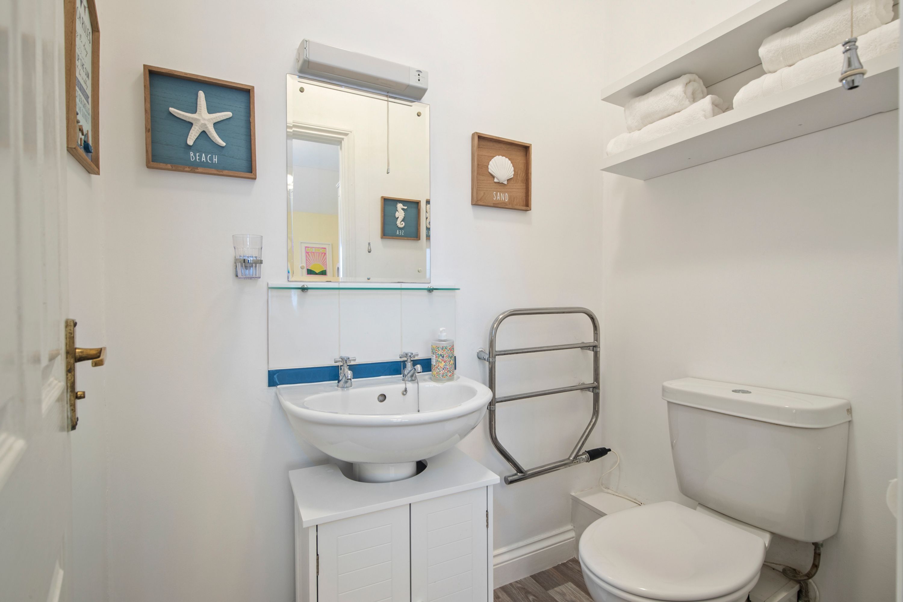 A bathroom with a white sink, mirror, and toilet. There are framed pictures on the wall and a towel rack above the toilet.