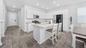 Una cocina moderna con armarios blancos, una isla central y un comedor con mesa y sillas de madera.