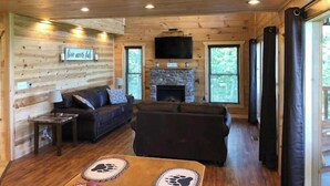 A cozy cabin interior with a stone fireplace, wooden walls, a sofa, and a television mounted on the wall. - Epic Mountain Views above Dollywood HotTub&ResPool (Sevierville)