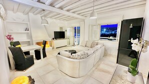 A modern living room with a white sofa, a dining area, and a TV.