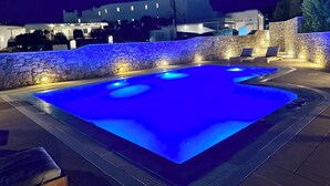 A nighttime swimming pool with blue lighting, stone walls, and lounge chairs.
