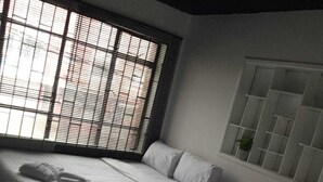 A bedroom with two beds, a window with blinds, and a built-in shelf with a plant. - HOTEL CAPITAL (Bogotá)