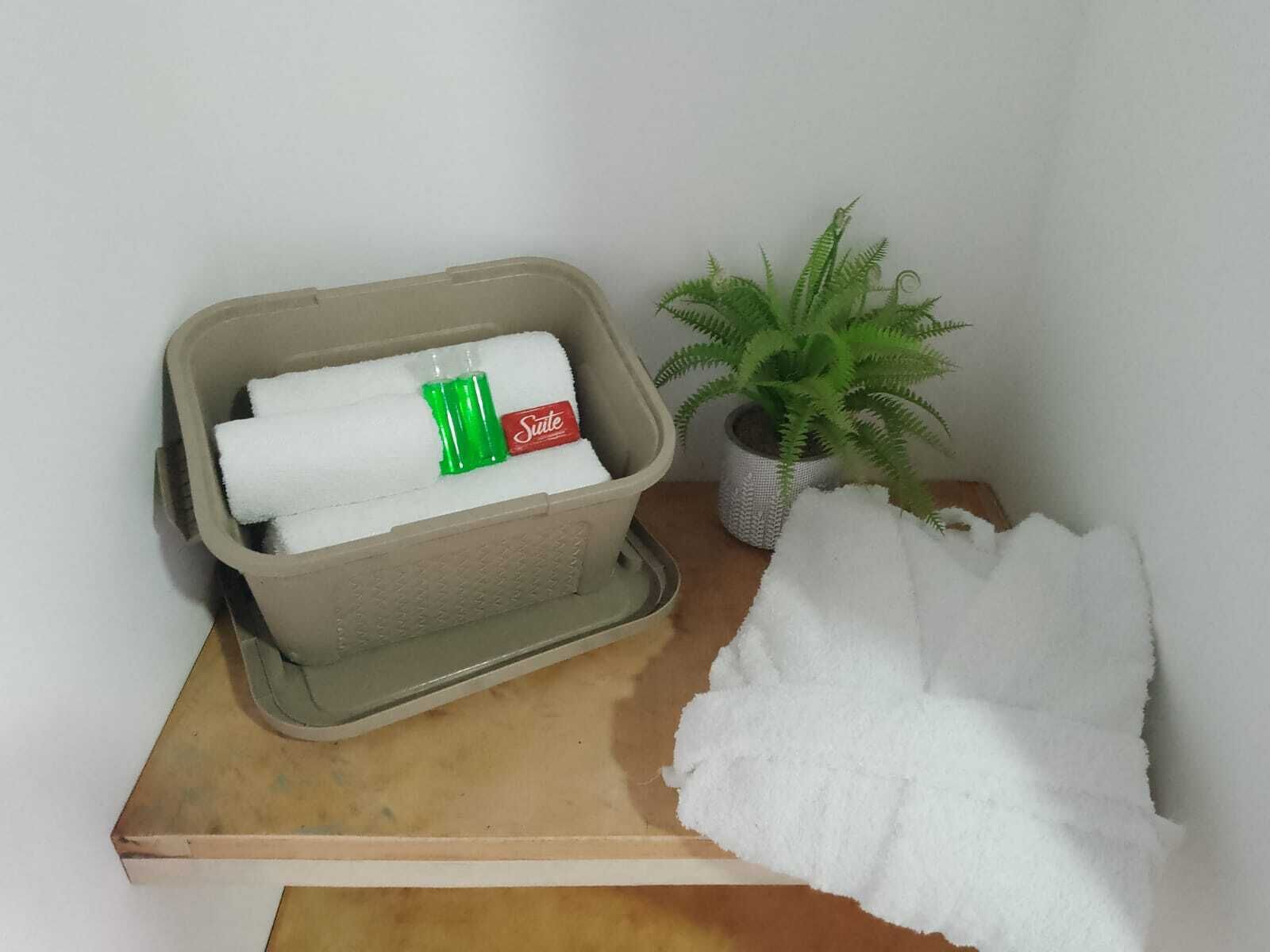 A beige plastic container with a white towel and a green bottle, a potted plant, and a pile of white towels on a wooden surface.
