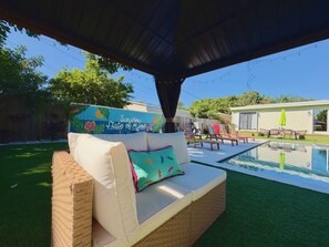 Un área de estar al aire libre techada con piscina, un muro decorativo y un paraguas de color verde brillante.