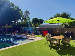 Un jardin avec une piscine, du gazon synthétique, du mobilier d’extérieur et une clôture en bois.