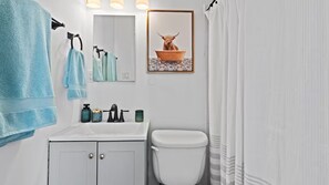 Ein Badezimmer mit Waschbecken, Spiegel, Toilette und Duschvorhang.