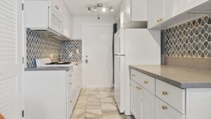 A narrow kitchen with white cabinets, a marble floor, and a patterned backsplash. - Waikiki Marina Ocean View Studio w/ Parking (Honolulu)