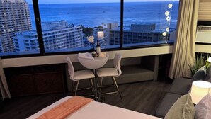 A hotel room with a large window offering a view of the ocean and cityscape. - Waikiki Marina Ocean View Studio w/ Parking (Honolulu)