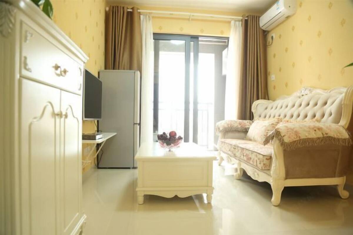 A living room with a sofa, a television, a small table with a vase, and a sliding glass door leading to a balcony.