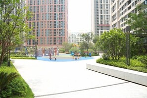 A playground area with play equipment, surrounded by greenery and adjacent to tall residential buildings. - She&He Apartment Hotel (Shenzhen Science Park) (Shenzhen)
