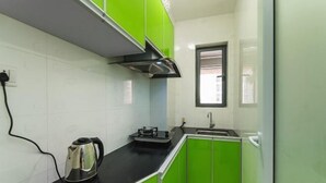 A compact kitchen with a black countertop, a stainless steel kettle, and green cabinets. - She&He Apartment Hotel (Shenzhen Science Park) (Shenzhen)
