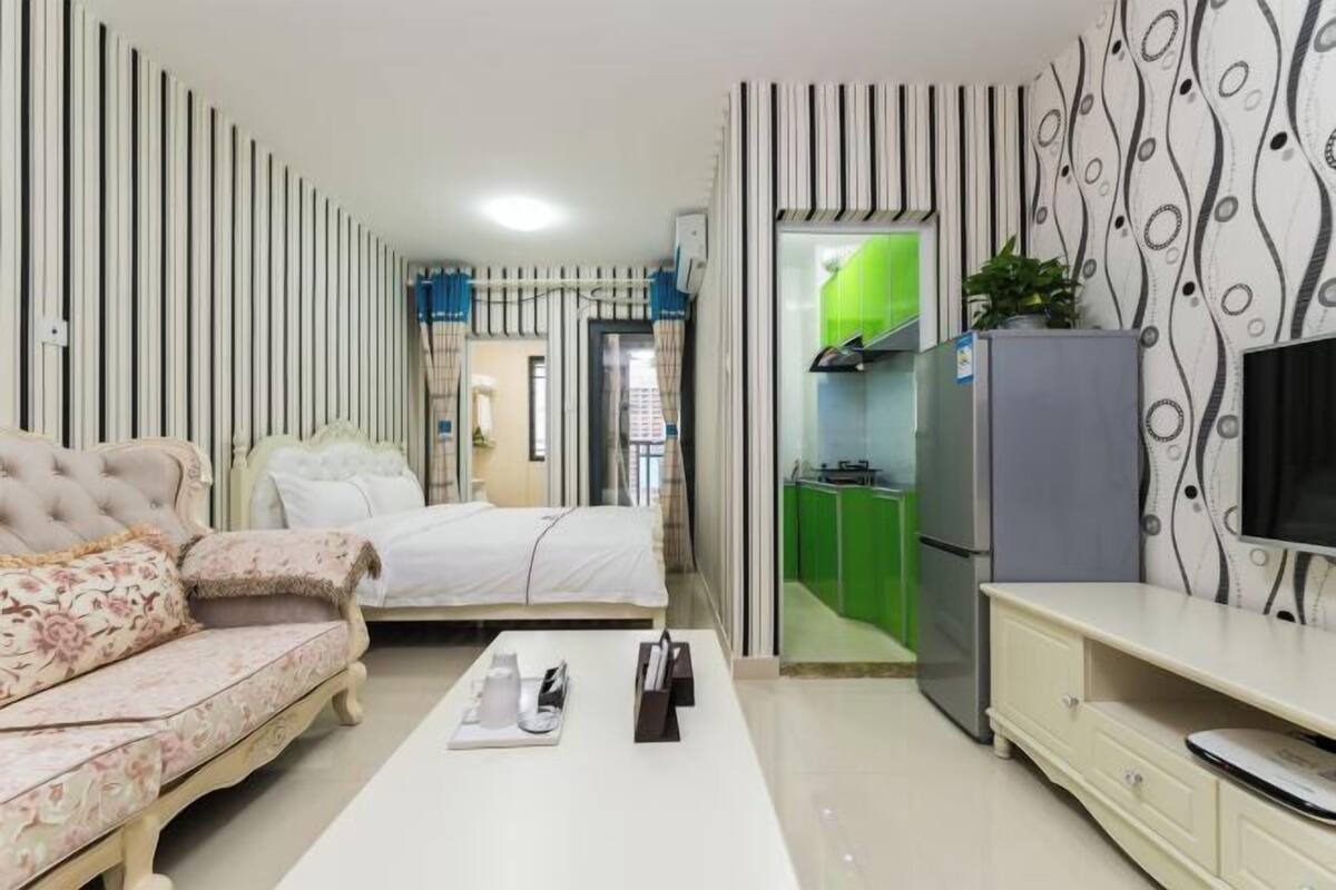A compact room with a bed, a sofa, a TV, a small kitchen area, and a dining table.