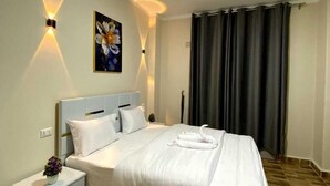 A neatly made bed in a hotel room with a headboard, bedside tables, and a painting on the wall. - Sky light hotel (Cairo)