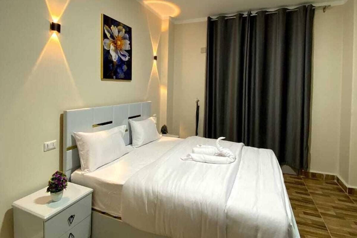 A neatly made bed in a hotel room with a headboard, bedside tables, and a painting on the wall.