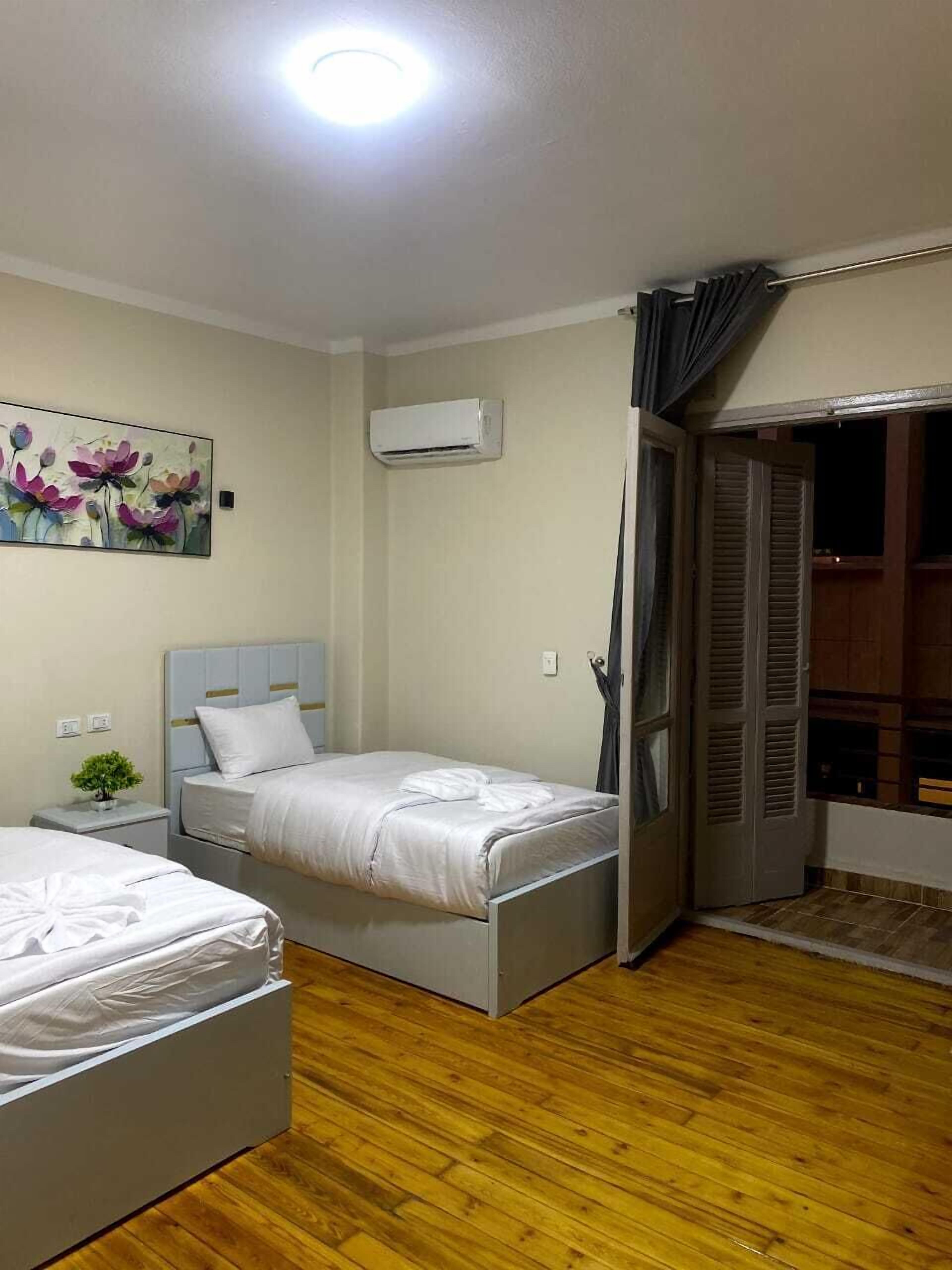 A bedroom with two beds, an air conditioning unit, a painting, and a sliding door to a balcony.