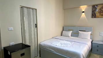 Habitación de hotel con cama, mesita de noche, armario y un refrigerador pequeño.