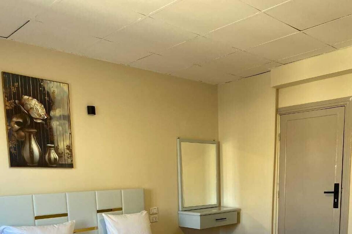 A neatly arranged hotel room with a large bed, a bedside table, a nightstand, a wall-mounted mirror, and a door.