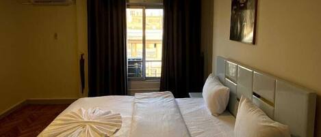 A hotel room with a bed, a nightstand, a painting on the wall, and a window with curtains.