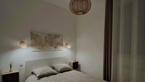 A modern bedroom with a large bed, bedside tables, a wall-mounted artwork, and a hanging light fixture. - Cosy apartment (Tarare)
