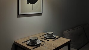 A dining area with a table set for two, a framed abstract artwork above, and a hanging pendant light. - Cosy apartment (Tarare)