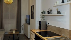 A modern kitchen with a built-in oven, a sink, and a coffee machine. There is a dining area with a table and chairs, and a living room with a sofa and a TV. - Cosy apartment (Tarare)