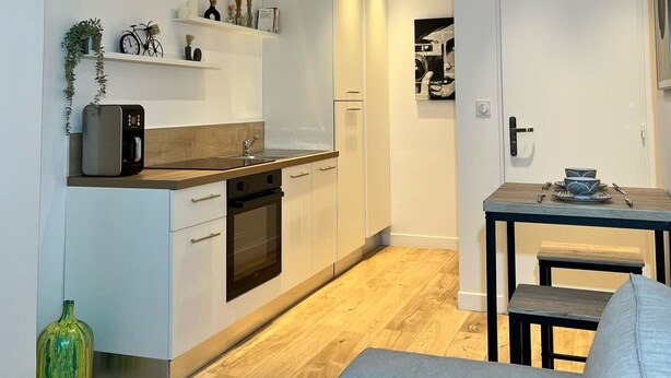A modern kitchen with white cabinets, a wooden countertop, and a built-in oven. There is a dining table with a bench and a hanging light fixture. - Cosy apartment (Tarare)